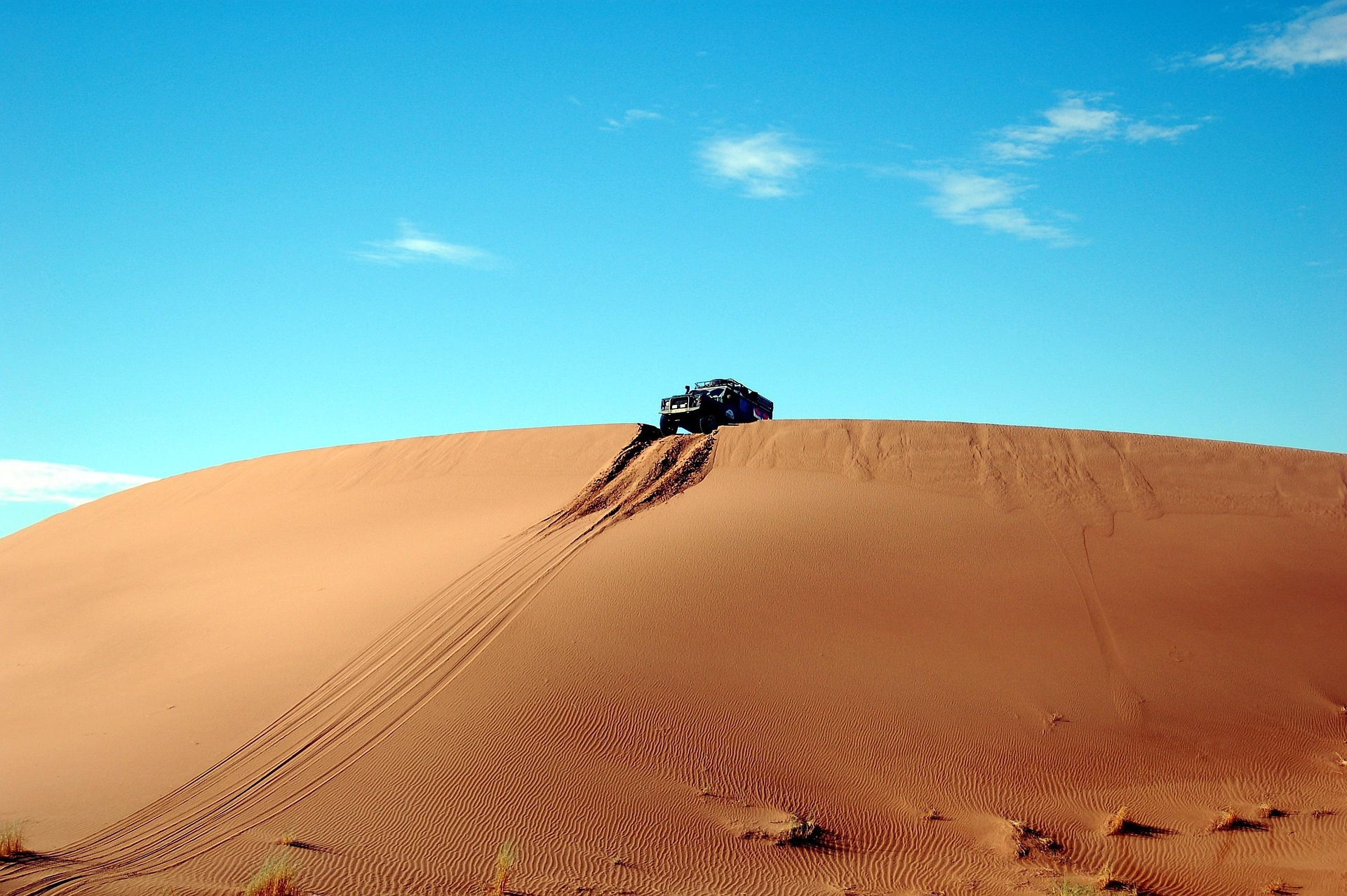 Un véhicule tout-terrain au sommet d’une dune, traces dans le sable